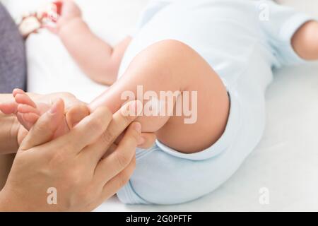 La mère applique de la crème au bébé garçon qui aide à maintenir l'hydratation de la peau des jambes, les soins de la peau et le concept de crème hydratante Banque D'Images