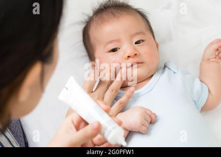 La mère applique de la crème au bébé garçon, ce qui aide à maintenir l'hydratation de la peau du visage, les soins de la peau et le concept de crème hydratante Banque D'Images