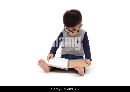 Portrait d'un adorable petit garçon asiatique portant des lunettes et lecture d'un livre isolé sur fond blanc Banque D'Images