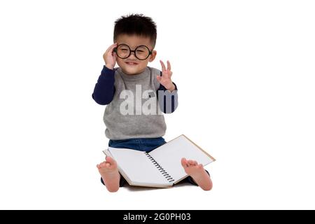 Portrait d'un adorable petit garçon asiatique portant des lunettes et lecture d'un livre isolé sur fond blanc Banque D'Images