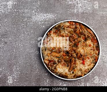 Nouilles de riz à la viande et aux légumes sur une assiette ronde sur fond sombre. Vue de dessus, plan d'appartement Banque D'Images
