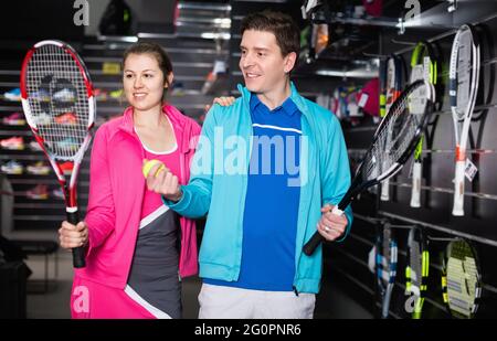 Le couple sportif en uniforme est démonstratrice d'une nouvelle fusée et d'un nouveau ballon pour le tennis Banque D'Images