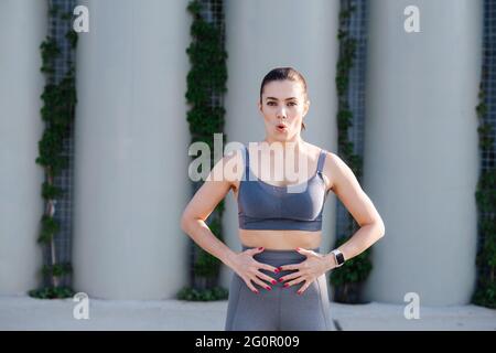 Femme concentrée s'exerçant dans la rue, faisant de l'exercice de respiration. Sur les montants de support. Haut gris et pantalon de yoga. Vue frontale. Banque D'Images