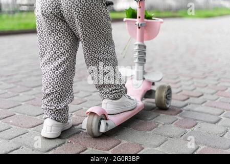 Enfants jambes sur le mini-scooter rose dans la ville européenne. En été, activités de plein air pour les enfants. Les tout-petits jouent dans les zones urbaines. Parentalité durable Banque D'Images