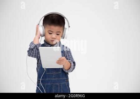 Portrait d'un petit enfant mignon satisfait tenant une tablette et écoutez de la musique sur une application isolée sur fond blanc Banque D'Images