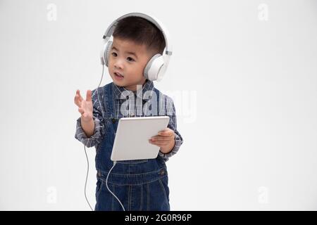 Portrait d'un petit enfant mignon satisfait tenant une tablette et écoutez de la musique sur une application isolée sur fond blanc Banque D'Images