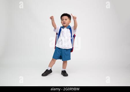 Petit garçon asiatique en uniforme d'étudiant avec sac à dos ayant l'amusement isolé sur fond blanc, première journée de maternelle et de Retour à l'école concept, thaï Banque D'Images