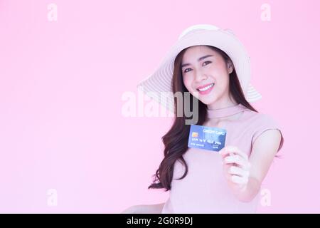 Belle jeune femme asiatique souriant et présentant carte de crédit avec copie espace fond rose, faisant le paiement pour les achats en ligne ou billet d'avion, E Banque D'Images