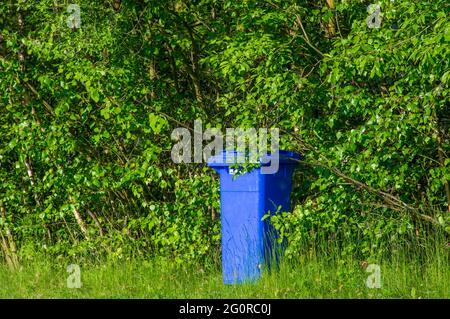 une poubelle bleue vide dans un parc public debout dans les buissons Banque D'Images