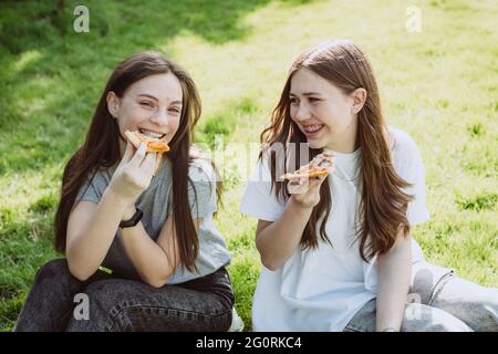 Deux jeunes amis joyeux dans le parc qui mangent de la pizza. Les femmes mangent de la nourriture rapide. Pas une alimentation saine. Mise au point sélective douce. Banque D'Images