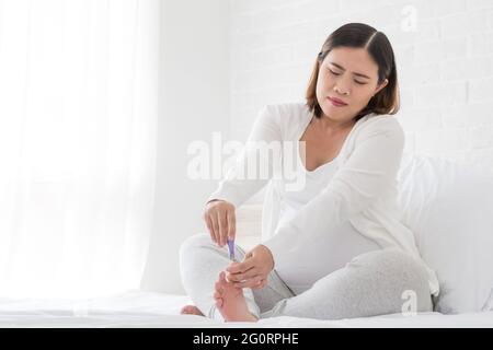 Femme enceinte pieds ongles coupe-ongles en blanc sur le lit dans la chambre, des soins de beauté pour les pieds et les ongles et manucure pendant la grossesse Banque D'Images