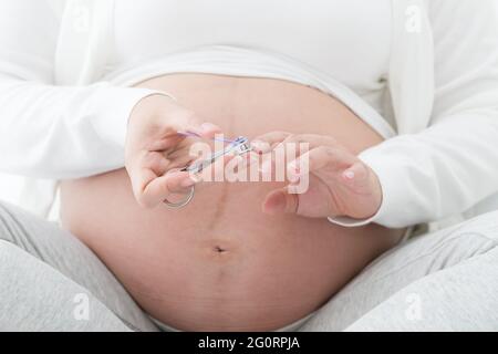 Femme enceinte main ongles coupe-ongles en blanc sur le lit dans la chambre, des soins de beauté pour le soin des ongles et manucure en bonne santé pendant la grossesse c Banque D'Images