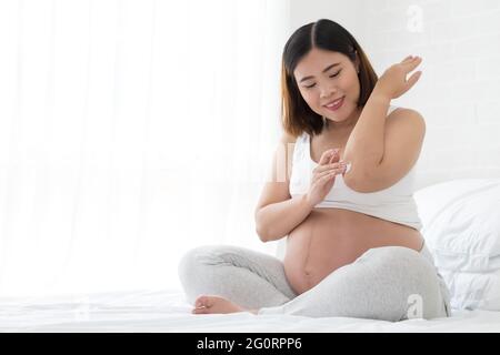 La femme enceinte prend soin du coude à l'aide de crème cosmétique, modèle asiatique Banque D'Images