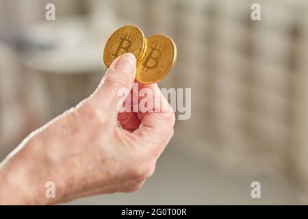 Une femme âgée tient des pièces de monnaie en bitcoin dans sa main. Concept d'homme âgé à la retraite heureux Banque D'Images