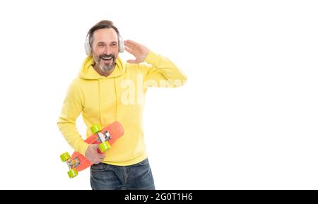joyeux homme mature skateboarder écouter de la musique porter des écouteurs tenir penny skateboard, dans la rue. Banque D'Images
