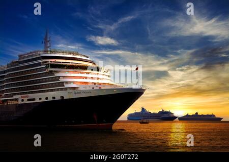 Le bateau de croisière Queen Victoria bénéficie d'un lever de soleil coloré à côté de Marella Explorer et Queen Mary 2 (à droite). Banque D'Images