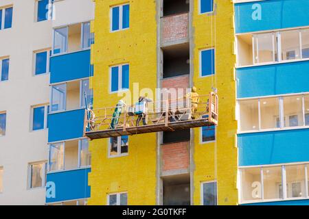 Les travailleurs sur une plate-forme mobile isolent les murs de la maison avec une isolation minérale. Banque D'Images