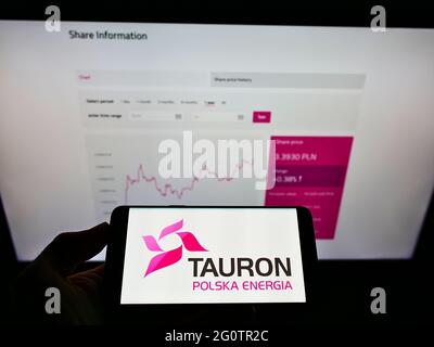 Personne tenant un smartphone avec le logo de la société polonaise d'énergie Tauron Polska Energia S.A. à l'écran devant le site. Mise au point sur l'affichage du téléphone. Banque D'Images