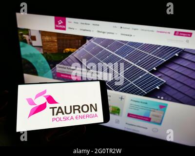 Personne tenant un téléphone portable avec le logo de la société polonaise d'énergie Tauron Polska Energia sa à l'écran en face de la page web d'affaires. Mise au point sur l'affichage du téléphone. Banque D'Images