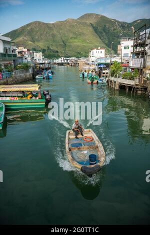 Un résident local conduit son bateau le long de la « route » principale du village de Tai O, île Lantau, Hong Kong Banque D'Images