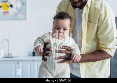 bébé en barboteuse tricotée entre les mains de père afro-américain Banque D'Images