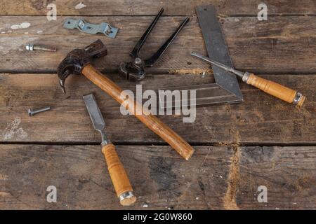 Quelques outils de menuisier sur une table en bois. Il y a un marteau, une paire de pinces, deux burins, un carré et des vis Banque D'Images