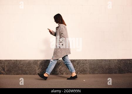 Vue latérale d'une femme transgenre utilisant un smartphone se tenant contre le mur Banque D'Images