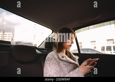 Femme non binaire utilisant un smartphone lors de ses déplacements en voiture Banque D'Images