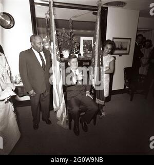 KN-C28776 29 mai 1963 le Président John F. Kennedy assiste à un anniversaire surprise tenu en son honneur par des membres du personnel de la Maison Blanche. Le valet du président Kennedy, George E. Thomas, est à gauche ; une femme non identifiée se trouve à droite. Visible sur la porte tout à droite : Ron Pontius, agent du service secret de la Maison Blanche, Evelyn Lincoln, secrétaire personnel du président Kennedy. Navy Mess Hall, White House, Washington, D.C. Veuillez indiquer « Cecil Stoughton. Photos de la Maison Blanche. John F. Kennedy Library and Museum, Boston Banque D'Images