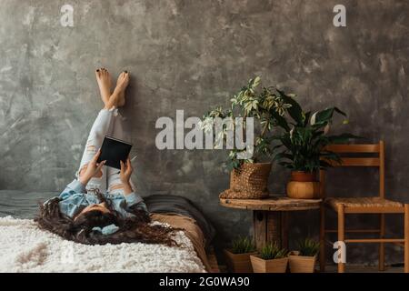 La femme se repose sur le lit avec ses jambes croisées, avec le livre dans ses mains. Banque D'Images