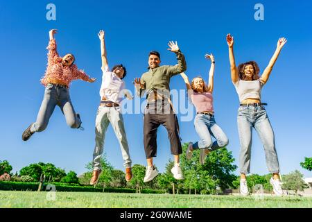 Groupe de jeunes heureux divers multi-raciaux amis de la génération z sautant ensemble en levant les bras et les jambes regardant la caméra. Concept de réussite et de vie du Banque D'Images