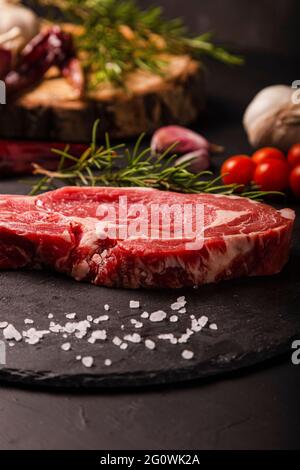 gros plan de steak de bœuf cru sur fond d'ardoise avec sel et herbes.