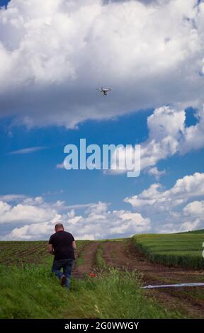 Un opérateur de drone capture des zones avec différentes variétés de céréales, d'orge, de blé et de maïs contre un ciel bleu avec des nuages blancs Banque D'Images