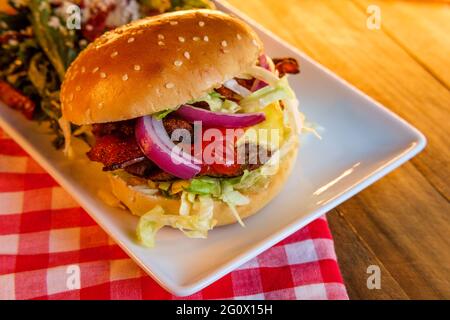 Cheeseburger de bœuf Angus recouvert de bacon croustillant servi avec une salade grecque Banque D'Images