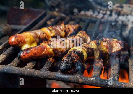 Hot-dogs au fromage enveloppé de bacon torréfiés sur du bois de feu de camp Banque D'Images