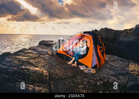 Femme assise dans la tente et travaillant sur ordinateur. Femme d'affaires travaillant de la plage. Concept de travail à distance. Travail et voyages de freelance o Banque D'Images