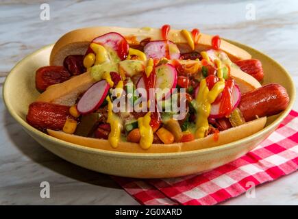 Chiens chipants de fantaisie recouverts de radis, de ketchup à la moutarde et de vert sauce sur des petits pains sans gluten Banque D'Images