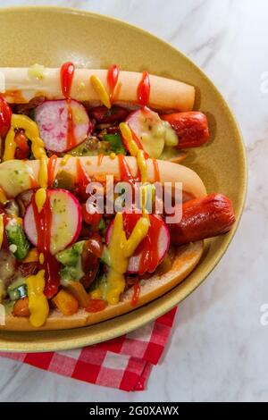 Chiens chipants de fantaisie recouverts de radis, de ketchup à la moutarde et de vert sauce sur des petits pains sans gluten Banque D'Images