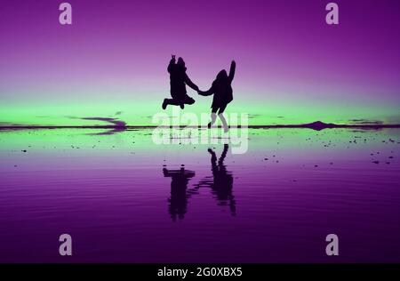 Pop art stylisé violet et vert couleur une silhouette de couple heureux sautant sur l'EFFET MIROIR de Uyuni Salt Flats en Bolivie, Amérique du Sud Banque D'Images