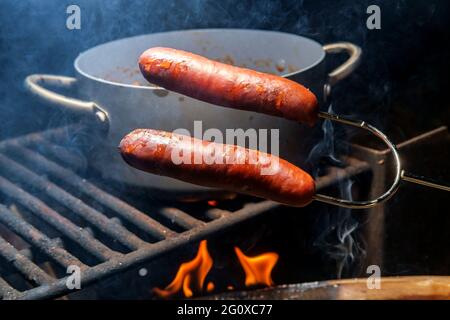 Torréfaction de bratwurst de feu de camp sur une fourchette pour chiens chauds avec des grains de cowboy ralenticuisiner en arrière-plan Banque D'Images