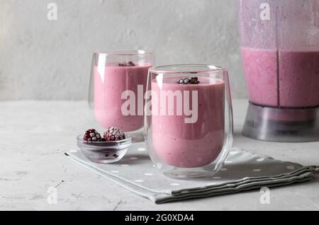 Smoothies aux mûres glacées dans deux verres transparents et bol mélangeur sur fond gris clair. Espace pour le texte Banque D'Images