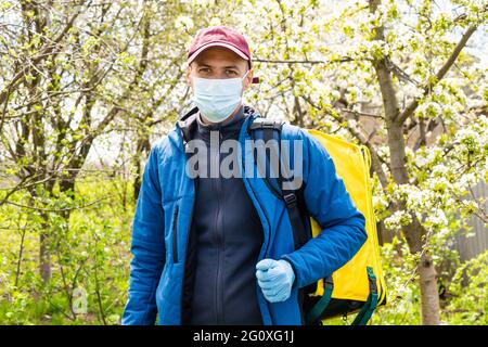 Jeune messager dans le masque médical livrant de la nourriture avec sac à dos thermique jaune dans la ville. Concept de service de livraison de nourriture Banque D'Images