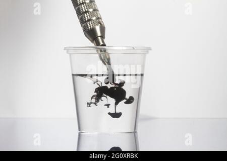 Machine à tatouer nettoyant les aiguilles à encre noire avec de l'eau propre dans du verre transparent Banque D'Images