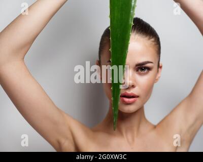 feuille d'aloès verte devant le visage d'une femme avec les mains soulevées sur un fond clair Banque D'Images