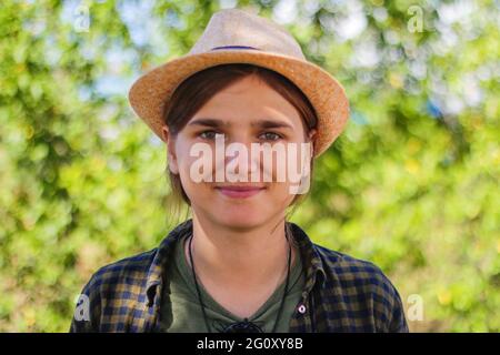 Feu de gros plan défoqué souriant jeune brune femme caucasienne en chapeau. Été flou vert nature bokeh arrière-plan. Portrait de beau jeune mignon Banque D'Images