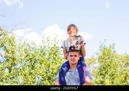 Frère défoqué de la sœur de circonscription à l'arrière. Portrait d'une fille heureuse sur les épaules de l'homme, porcgyback. Fille tenant chat, chaton. Famille jouant à l'extérieur. J'adore pe Banque D'Images