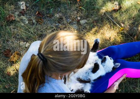 Flou blond petite fille jouant avec chat, noir et blanc petit chaton de relaxation. Nature vert fond d'été. Une fille qui s'en est à l'animal. Animaux d'amour Banque D'Images