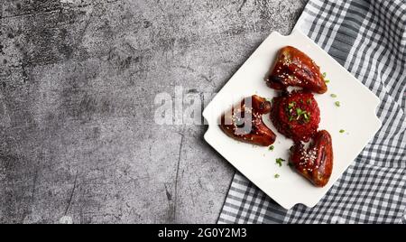 Ailes de poulet rôties avec risotto aux betteraves sur une assiette carrée sur fond gris foncé. Vue de dessus, plan d'appartement Banque D'Images