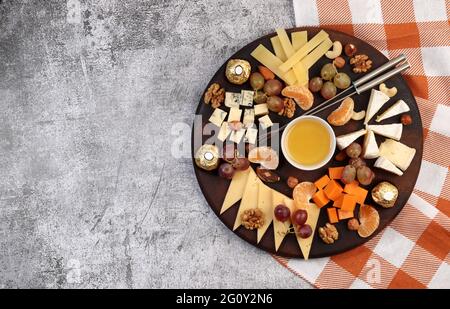 Plateau de fromages servi avec du miel, du raisin, des baies et des noix sur fond sombre. Vue de dessus, plan d'appartement Banque D'Images