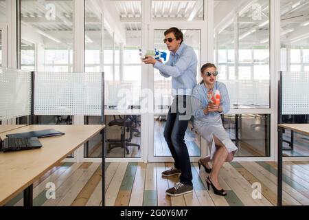 Homme et femme en costume habillé debout dos à dos et visant les armes à jouets tout en s'amusant au bureau Banque D'Images